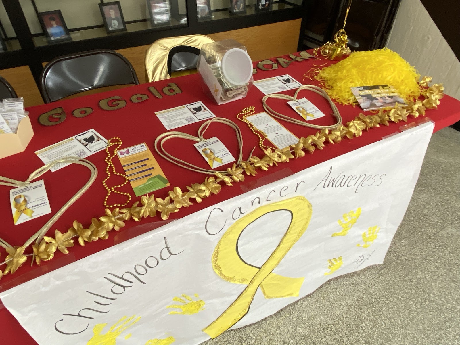 Table covered in red tablecloth with gold shoelaces and a banner saying "Childhood Cancer Awareness" 