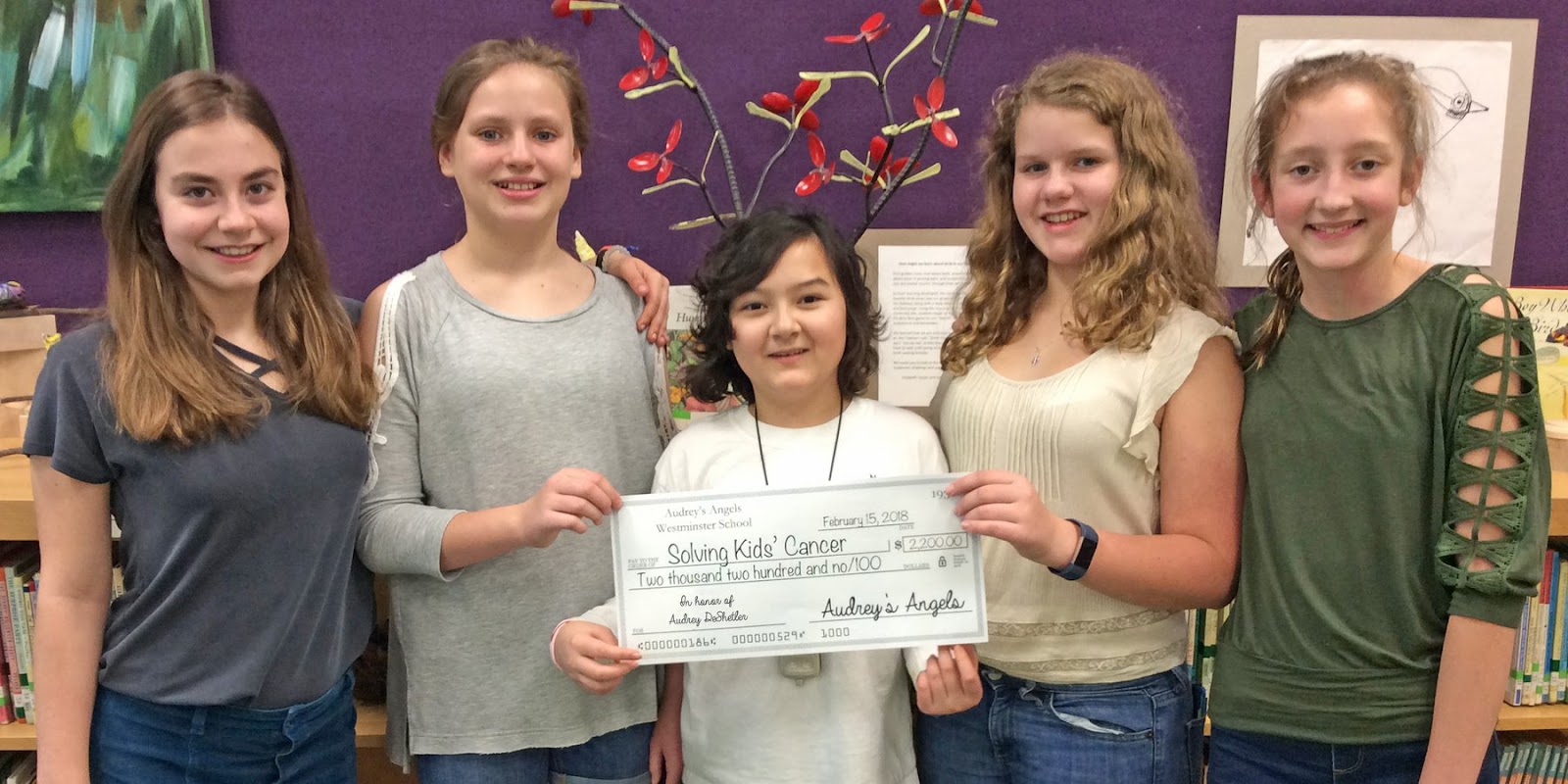 Photo: Audrey with her friends holding a check made out to Solving Kids Cancer signed by their childhood cancer fundraiser, Audrey's Angels.